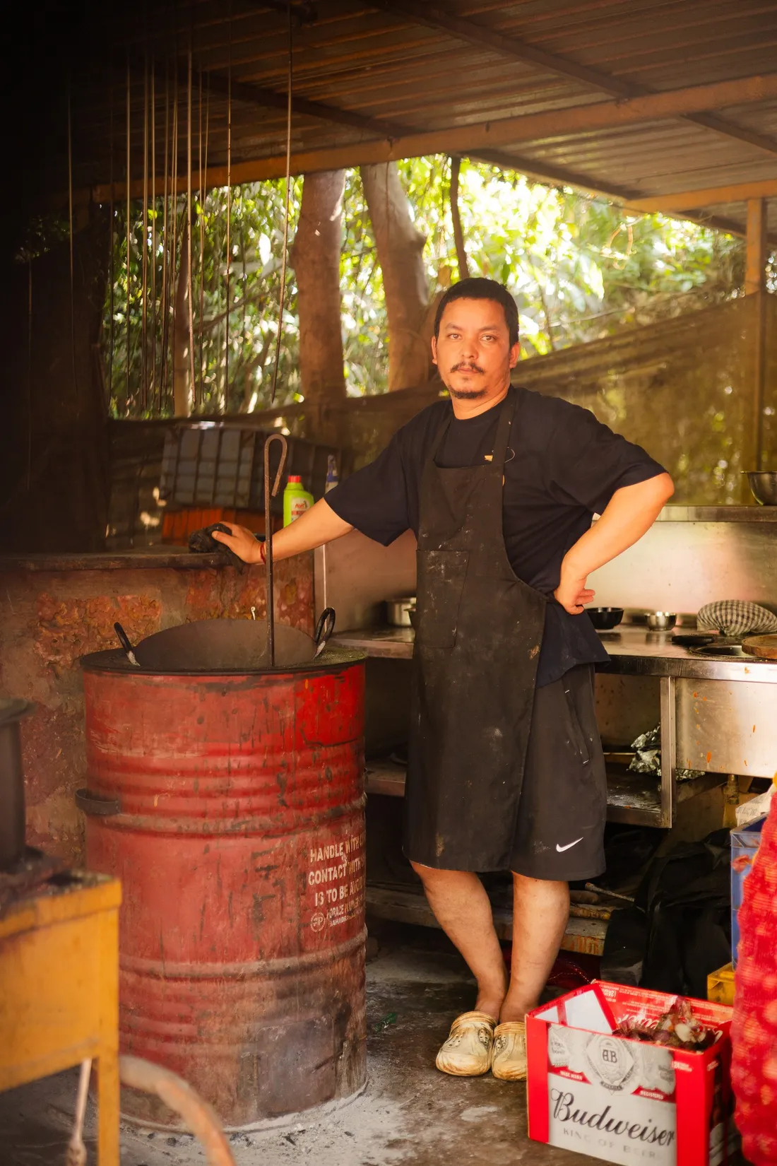 A cook standing at the drum tandoor in A2’s open kitchen, skewers hanging above it.