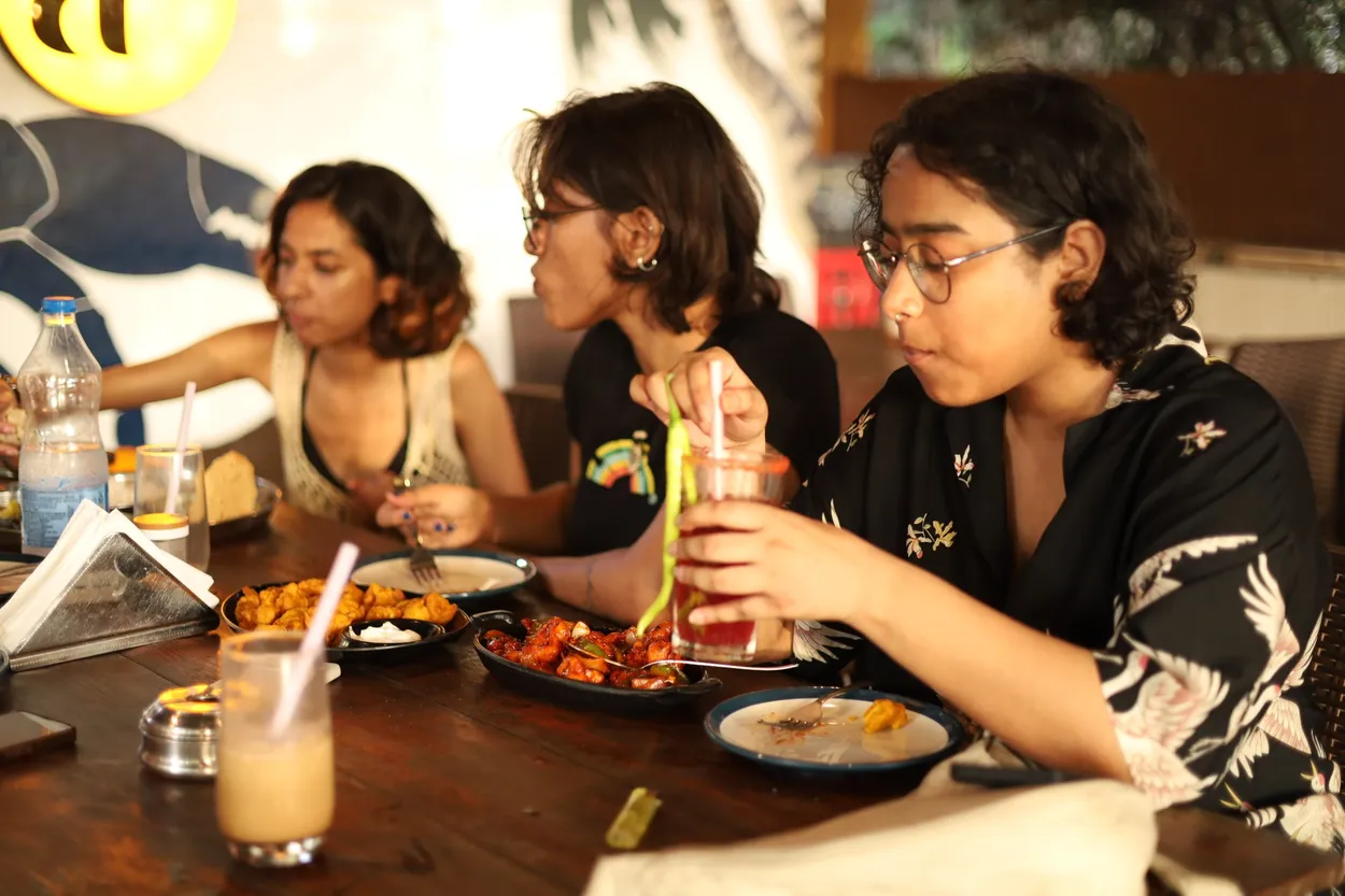 Three friends eating at a long wooden table under the yellow a² sign.